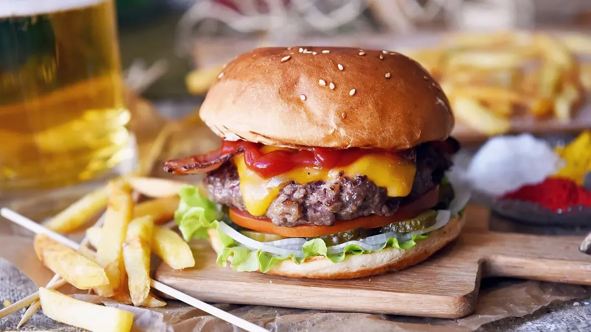 burger z sosem sałatą bułką na desce obok frytki