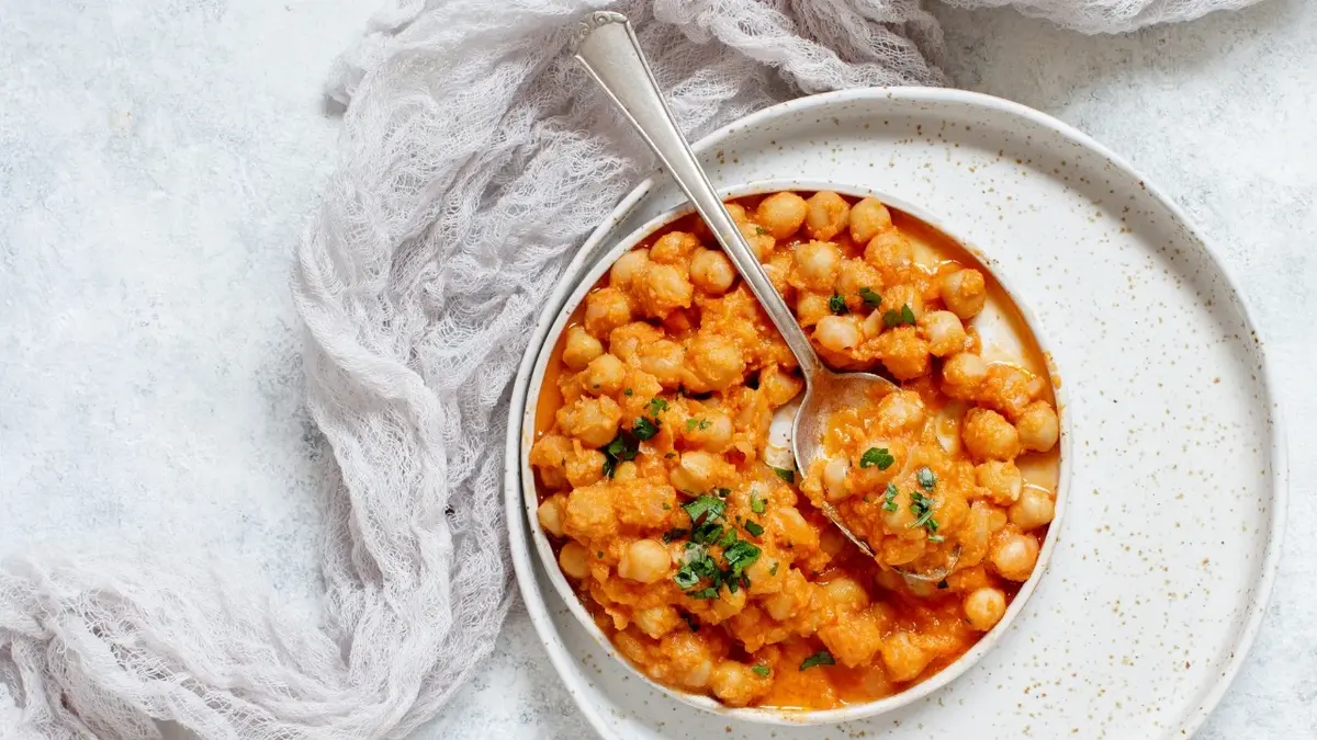 chana masala ciecierzyca z łyżką na białej tacy obok tkanina na białym tle