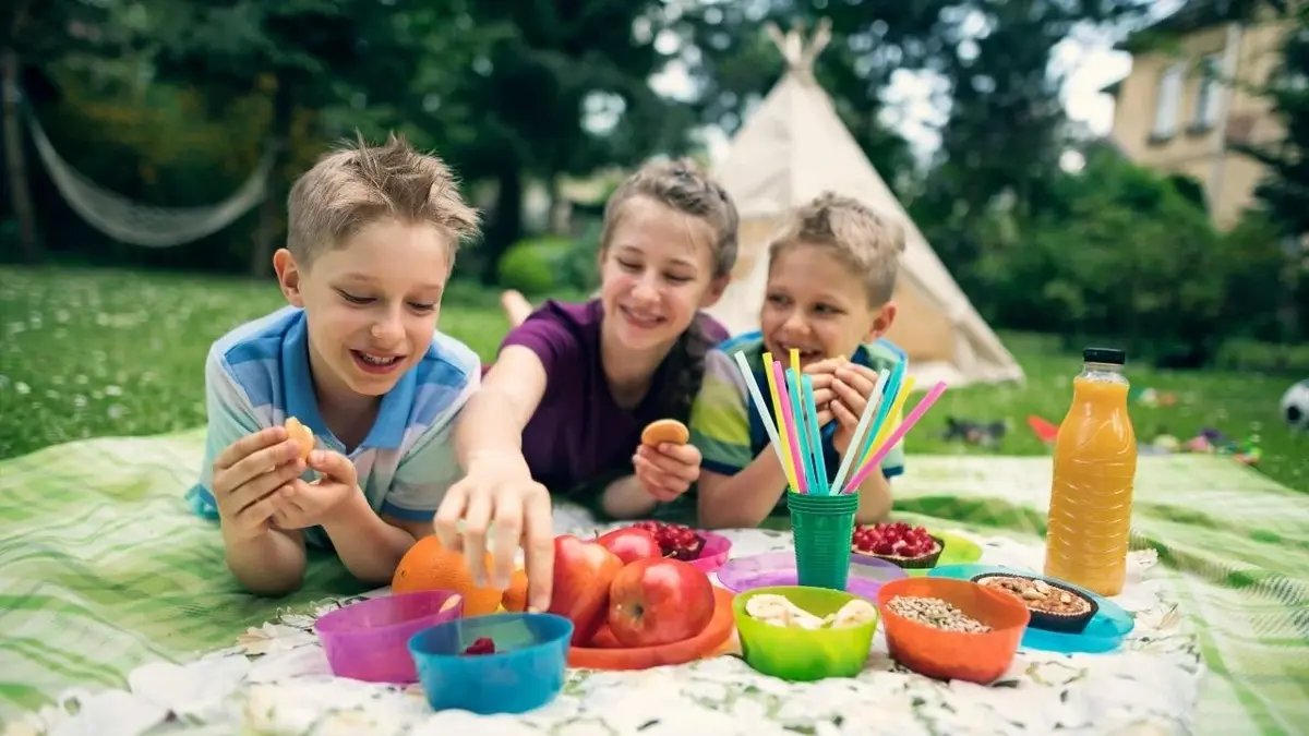 Troje dzieci na pikniku podczas majówki. Za nimi jest namiot.