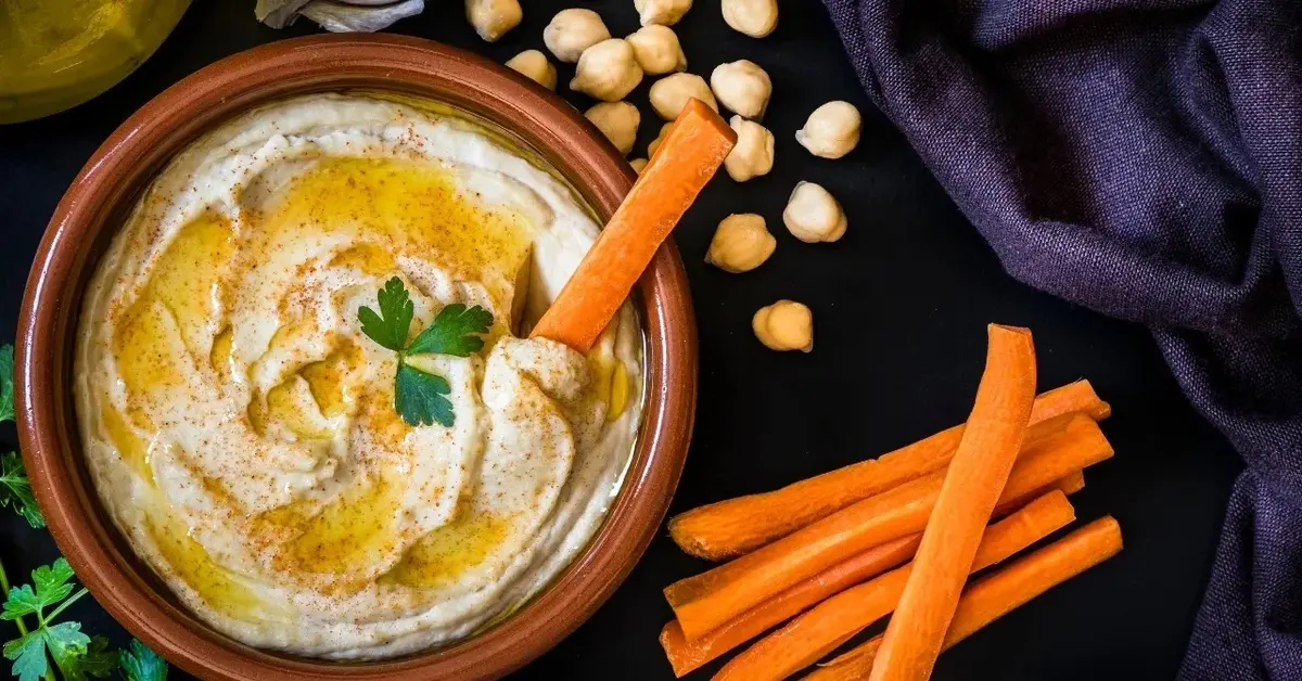 hummus z marchewką obok cieciorka słupki marchewki