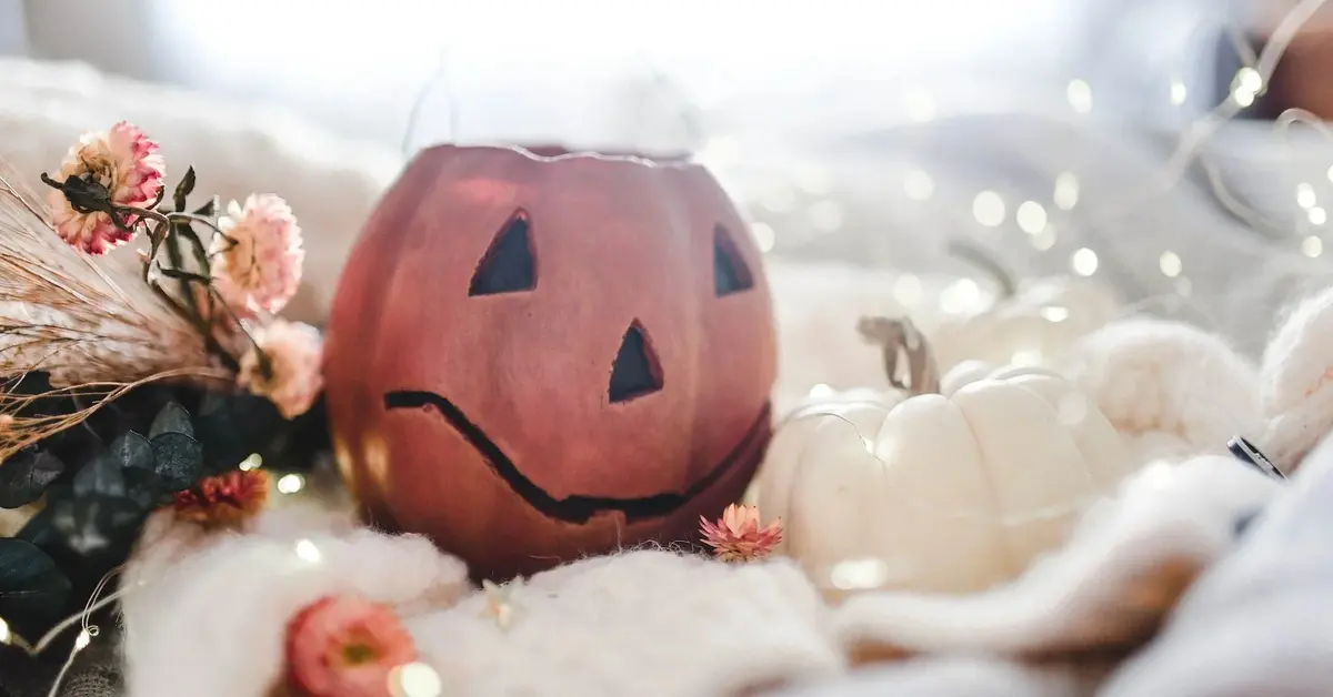 Stół z jesiennymi dekoracjami: światełkami, dynią halloween, herbacianymi różami