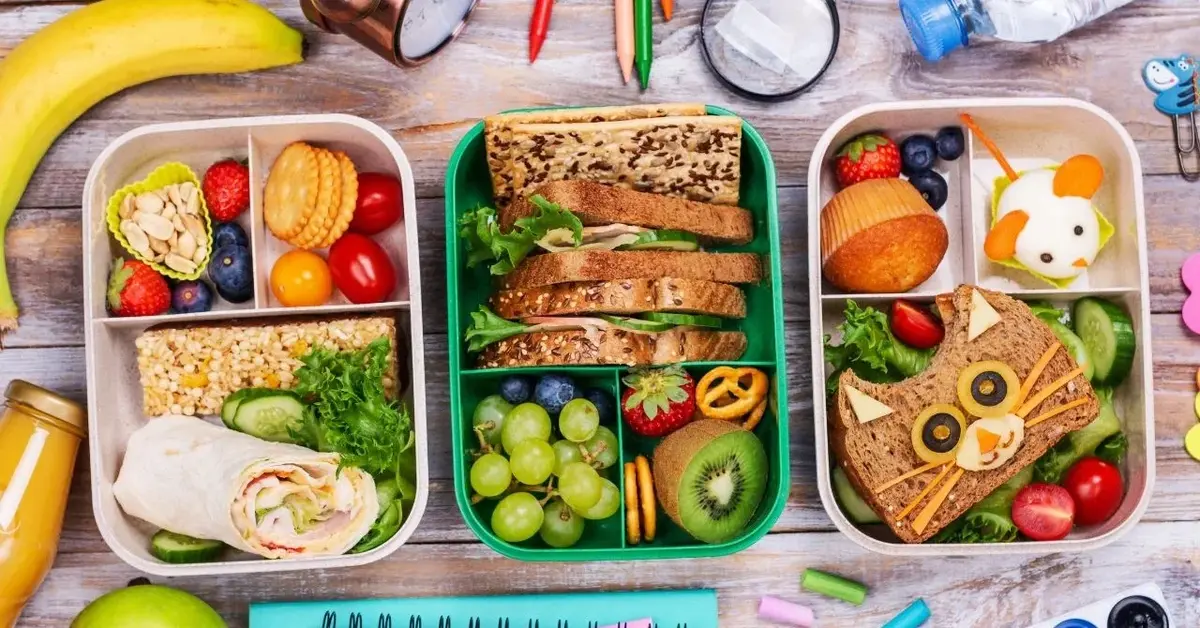 lunchboxy z różnymi przekąskami wokół przybory szkolne owoce, sok