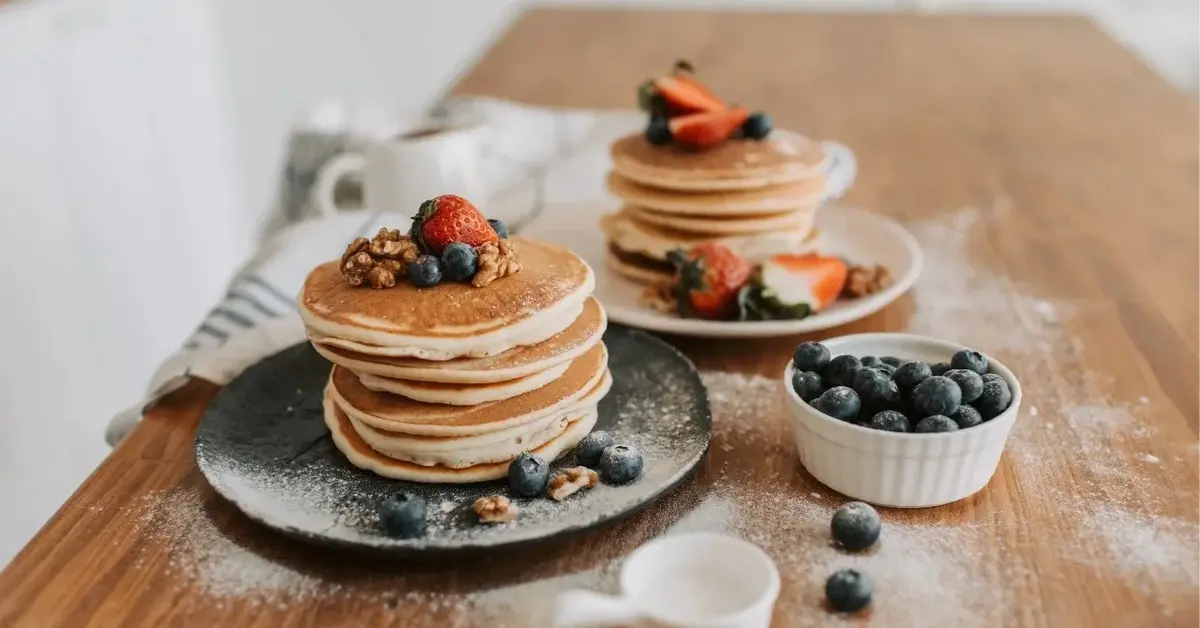 na dwóch talerzach wieże z pancakes'ow obok miseczka z borowkami