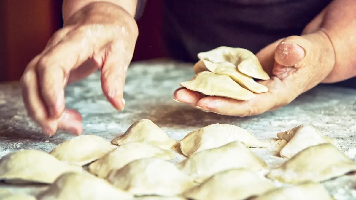 ręce podnoszą pierogi ze stolnicy