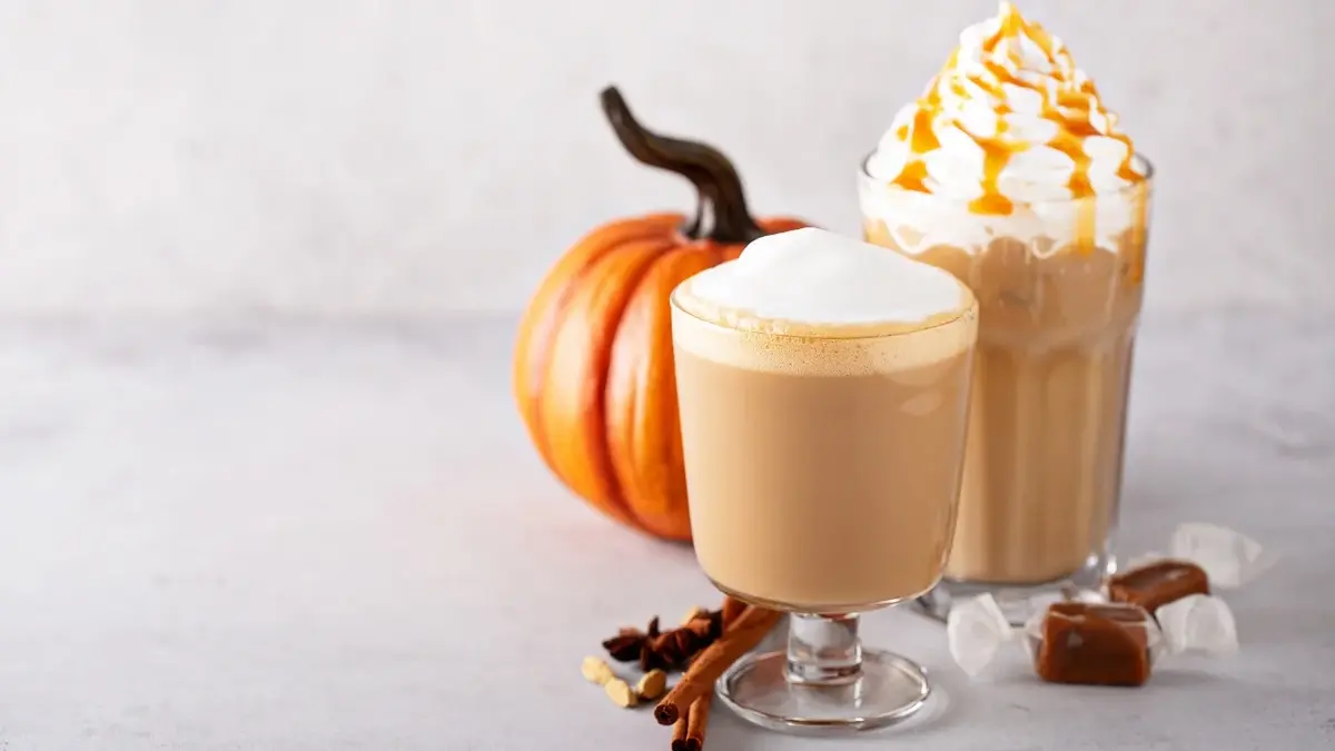 pumpkin spice latte kawa dyniowa w szklankach z bitą śmietaną z tyłu dynia na jasnym tle