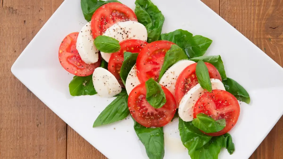 Sałatka caprese: bazylia, pokrojony pomidor i mozzarella pokrojona w plasterki.