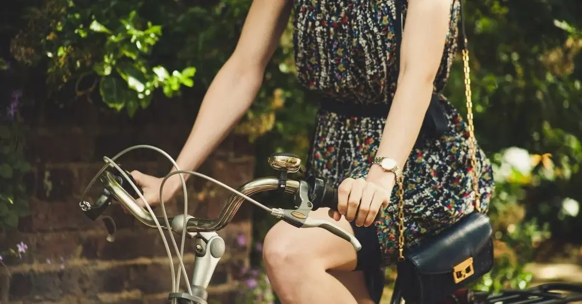 Kobieta w letniej sukience z torebką na łańcuszku jedzie na rowerze