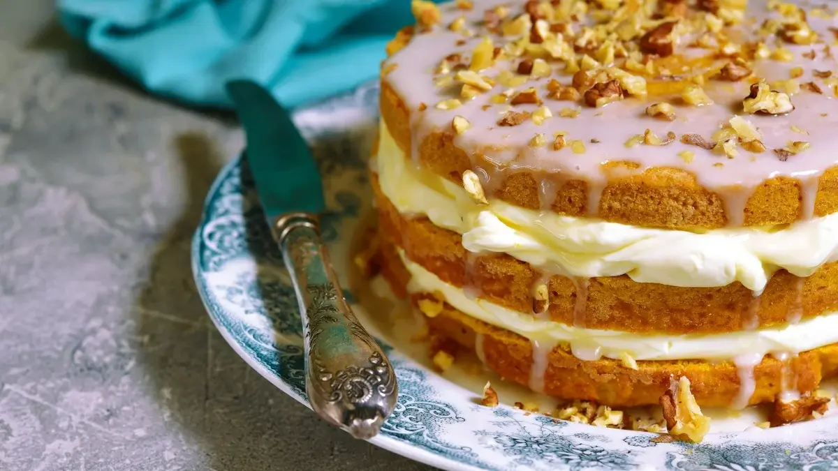 tort z mascarpone na zdobionym talerzu z nożem ścierka niebieska w tle tort ozdobiony różowym lukrem posypany orzechami