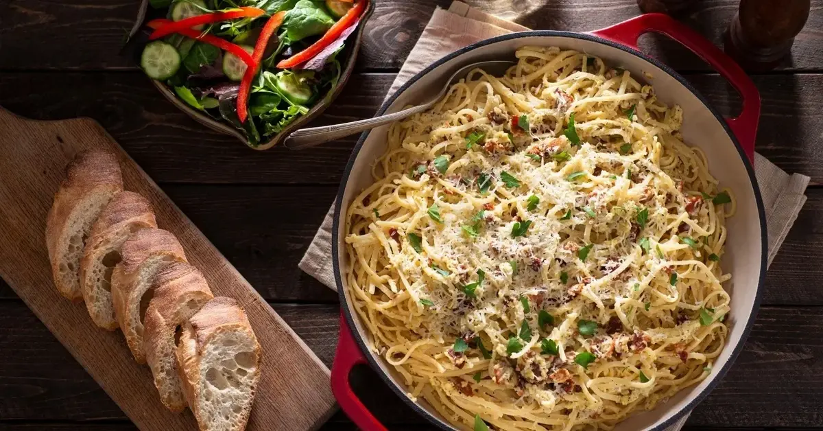 Carbonara ze szpinakiem na głębokim talerzu, dookoła dodatki: sałatka, kromki świeżej bagietki 