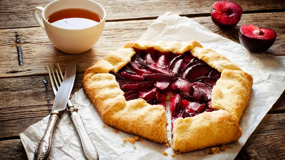 Galette ze śliwkami, obok kubek z herbatą i sztućce