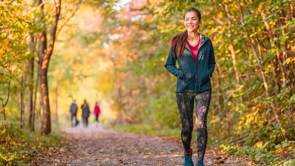 Kobieta w leginsach i sportowej kurtce spacerująca w lesie 