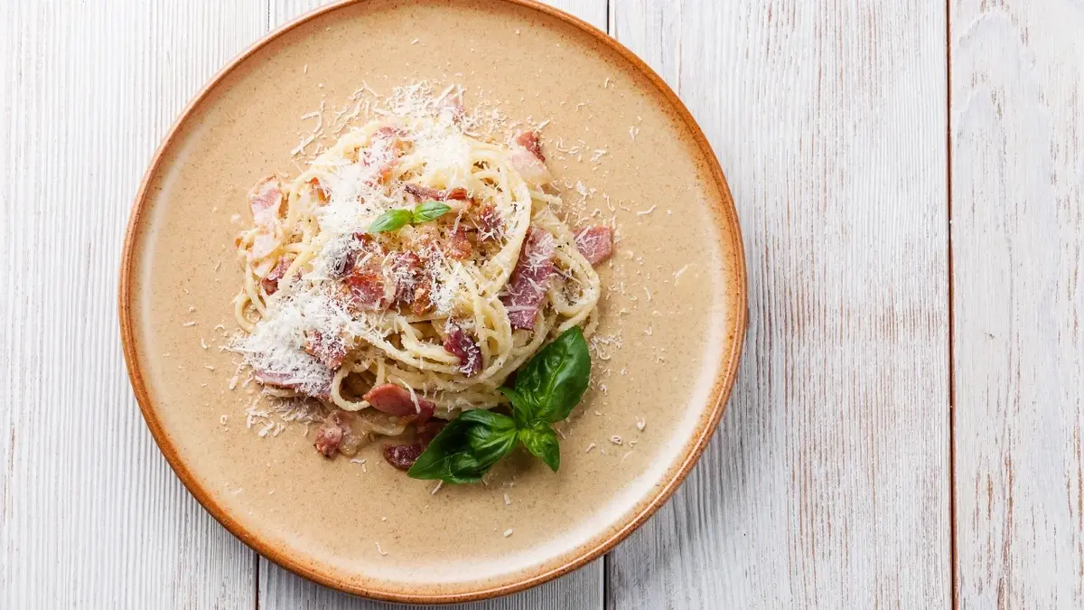 Carbonara ze szpinakiem posypana tartym parmezanem na talerzu 