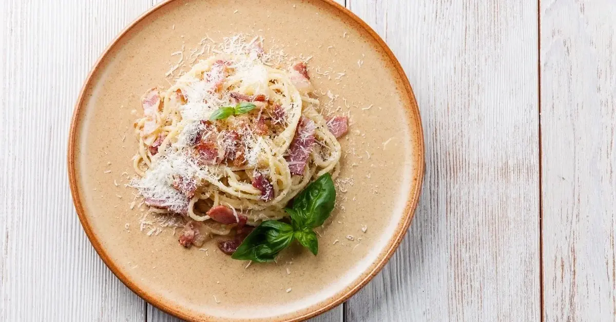 Carbonara ze szpinakiem posypana tartym parmezanem na talerzu 