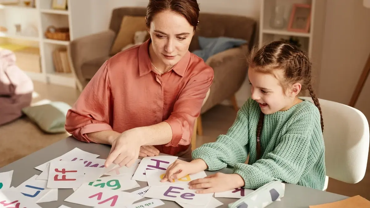 Mama i córka uczące się przy stole na którym leżą kartoniki z literami