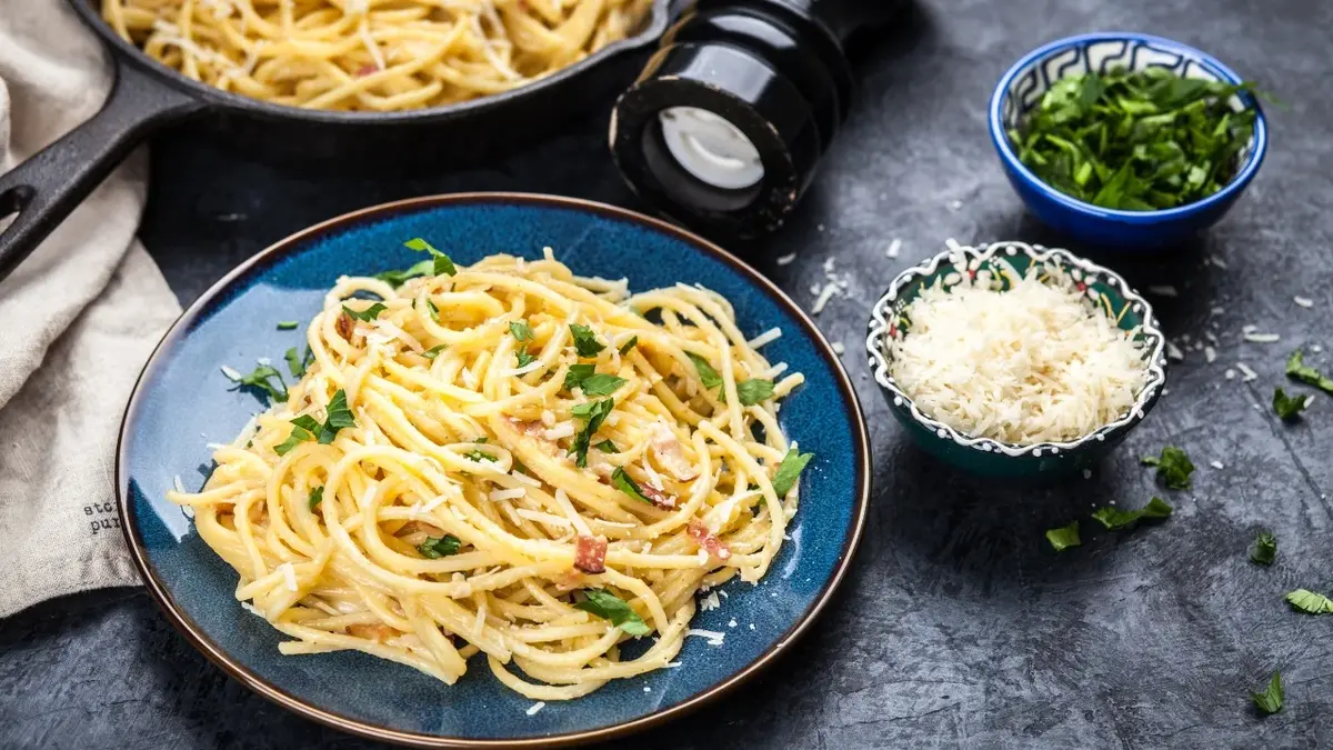 Carbonara ze szpinakiem na głębokim talerzu, dookoła dodatki: kromki świeżej bagietki, ser parmezan stary w miseczce