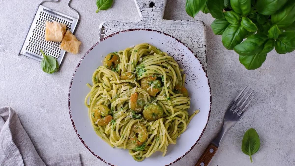 Kretki w sosie śmietanowym z makaronem spaghetti na białym talerzu. Obok tarka do sera i kawałek parmezanu