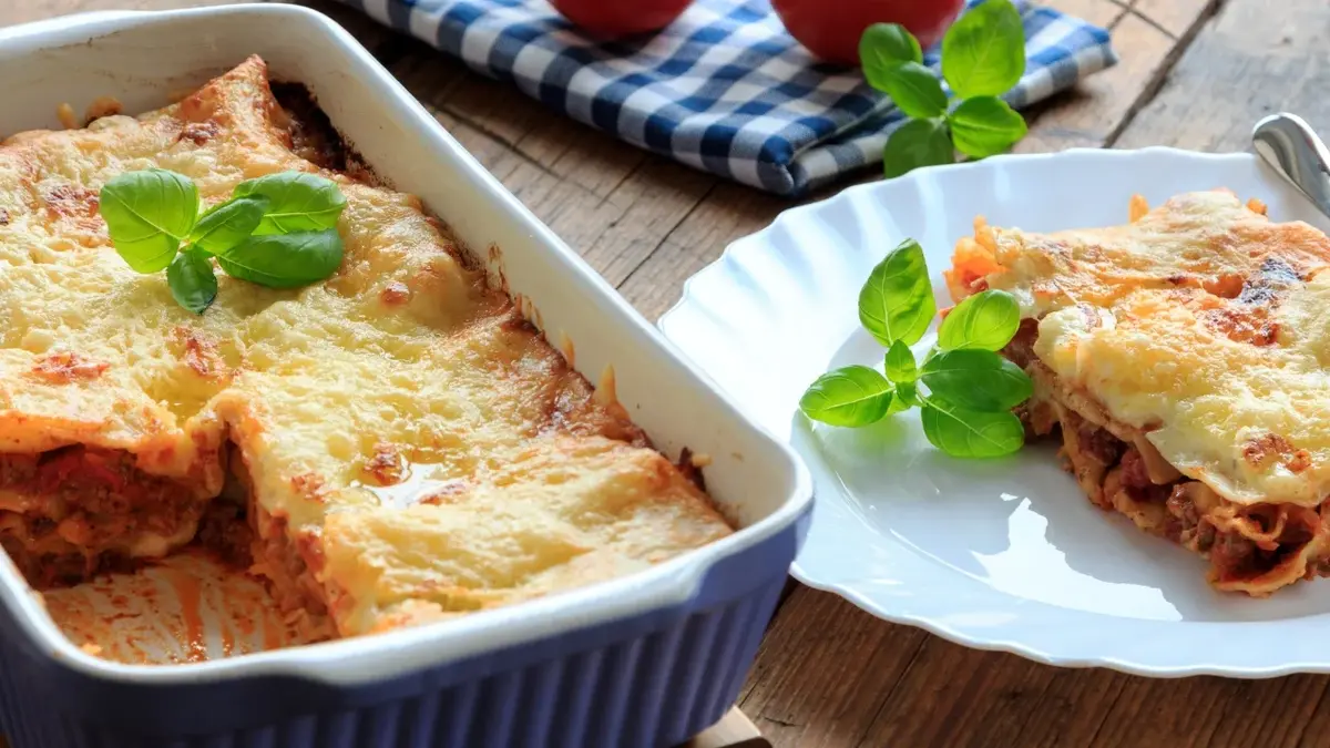 Lasagne w naczyniu do zapiekania i porcja na talerzu stojącym obok