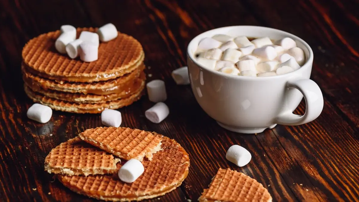 Wafle na drewnianym blacie. Obok filiżanka z czekoladą i piankami 