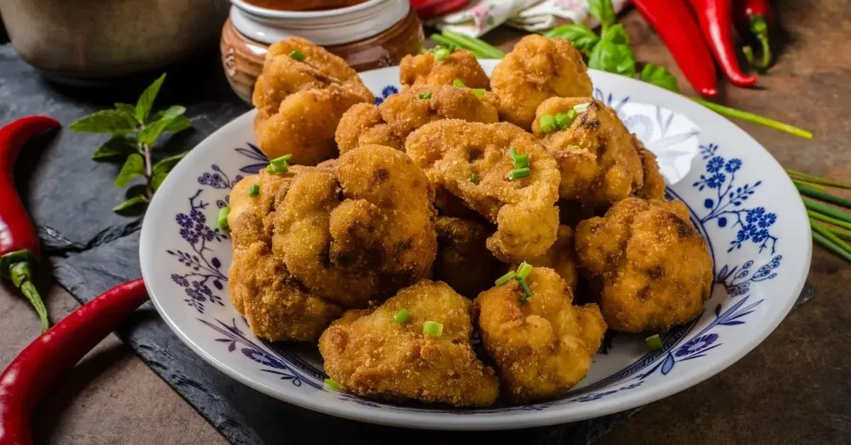 Różyczki kalafiora w panierce na talerzyku. Dookoła papryczki chilli, przyprawy