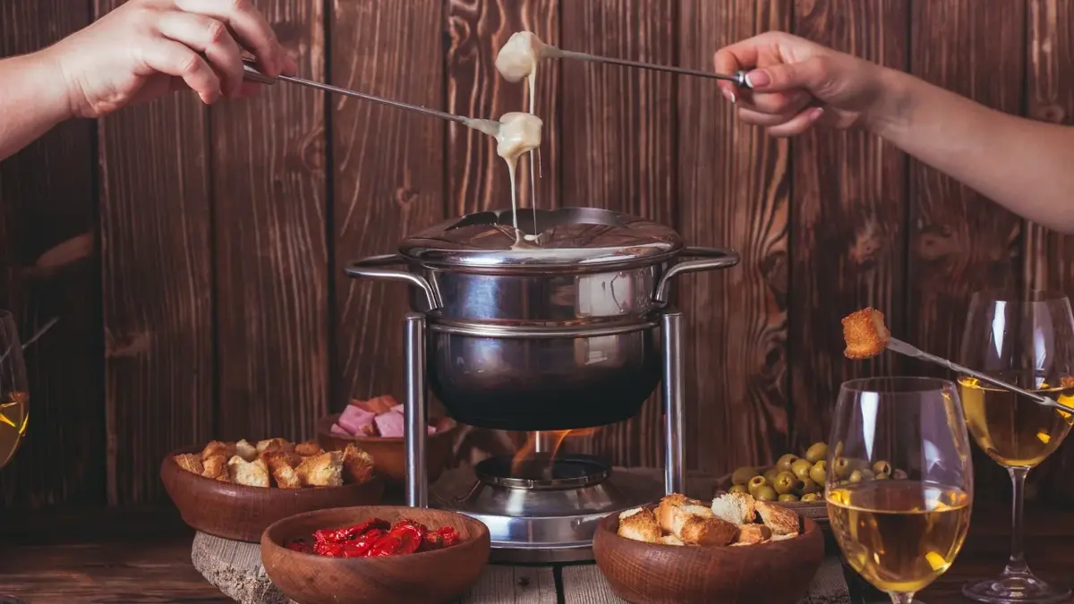 Srebrny garnek do fondue serowego. Dookoła dodatki 