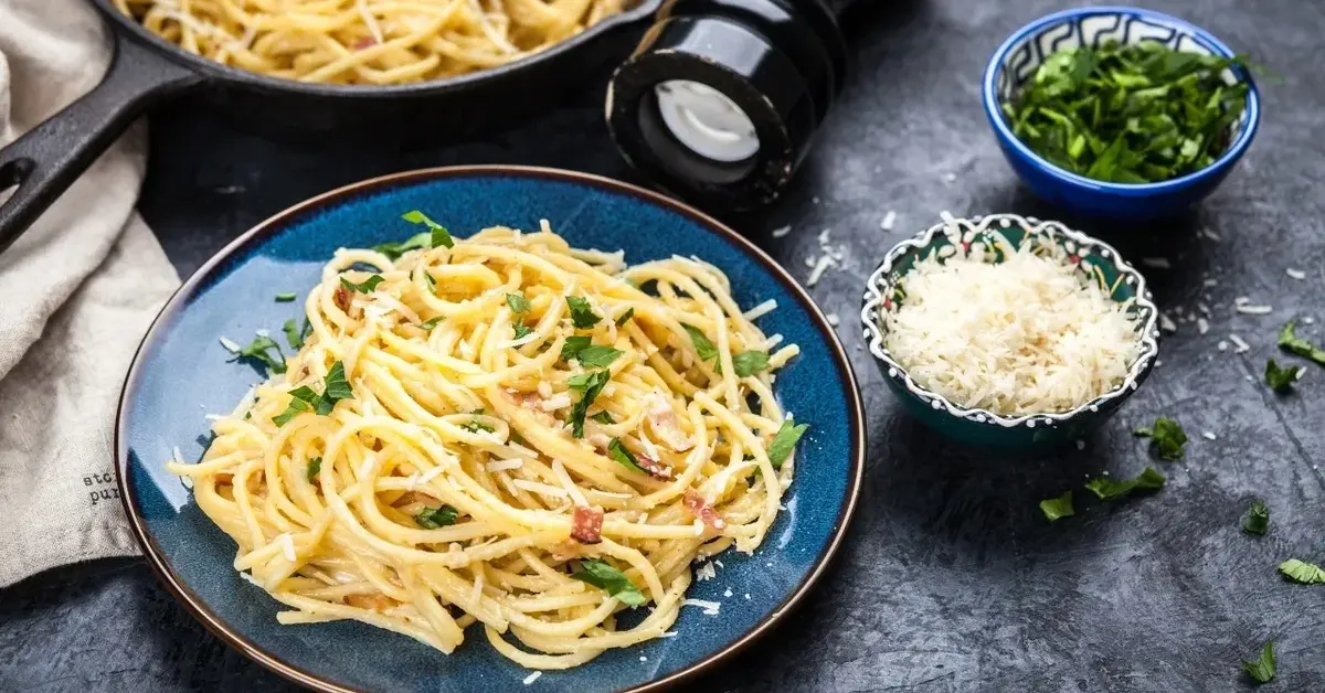 Wegańska Carbonara na niebieskim talerzu, obok dodatki w miseczkach 