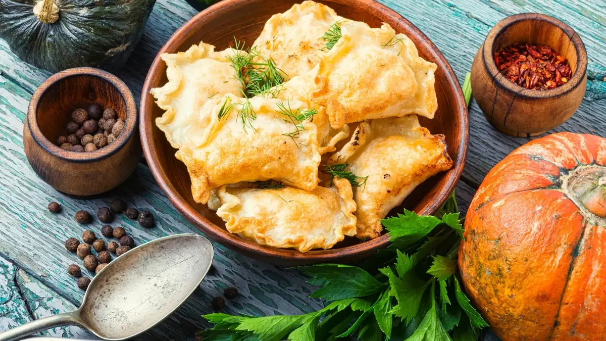 Pierogi z dynią w głębokiej misce, obok dynie w różnych kształtach 