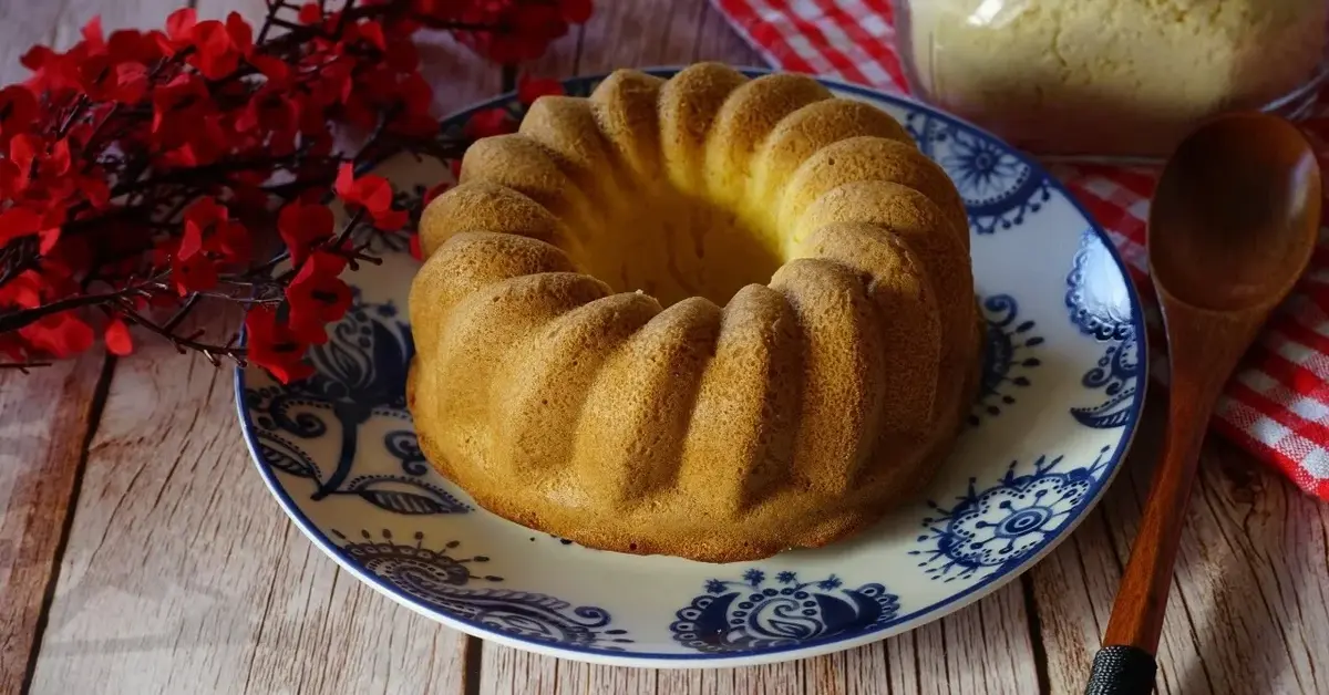 Babka drożdżowa na ozdobnym talerzu. Obok czerwone kwiaty