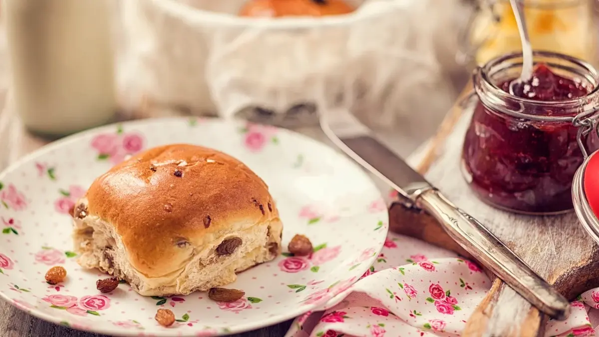 Bułeczka z rodzynkami na talerzyku w różyczki, obok słoiczek z dżemem