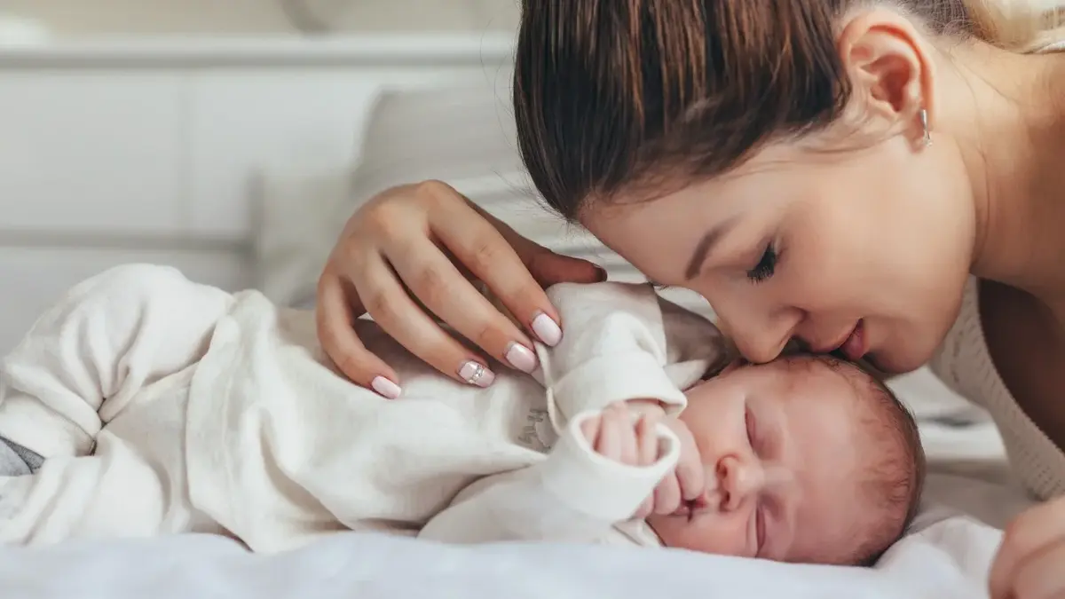 Śpiący niemowlak i pochylająca się nad nim mama