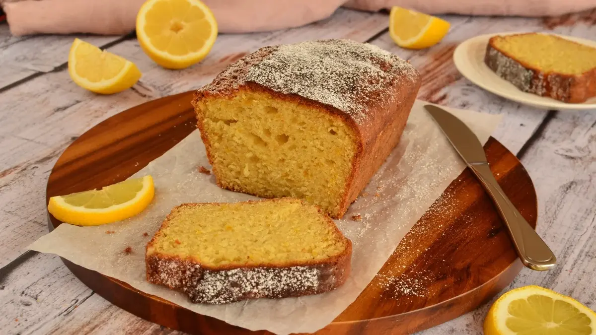 Babka cytrynowa i odkrojony jeden jej kawałek na brązowym talerzyku. Dookoła porozkładane plasterki cytryny