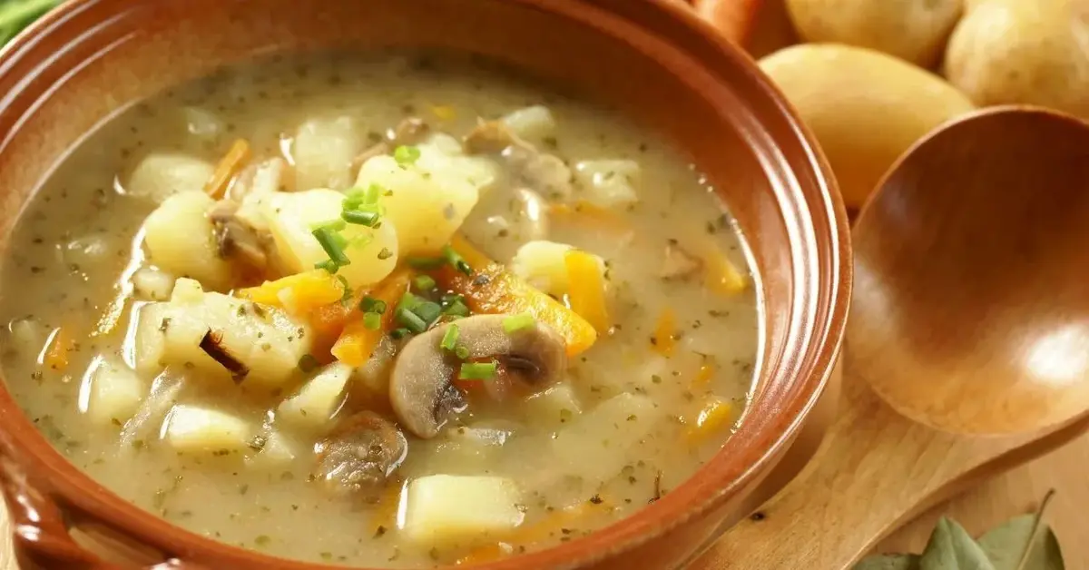 Zupa ziemniaczana z leśnymi grzybami podana w brązowej, rustykalnej misce, obok leży drewniana łyżka